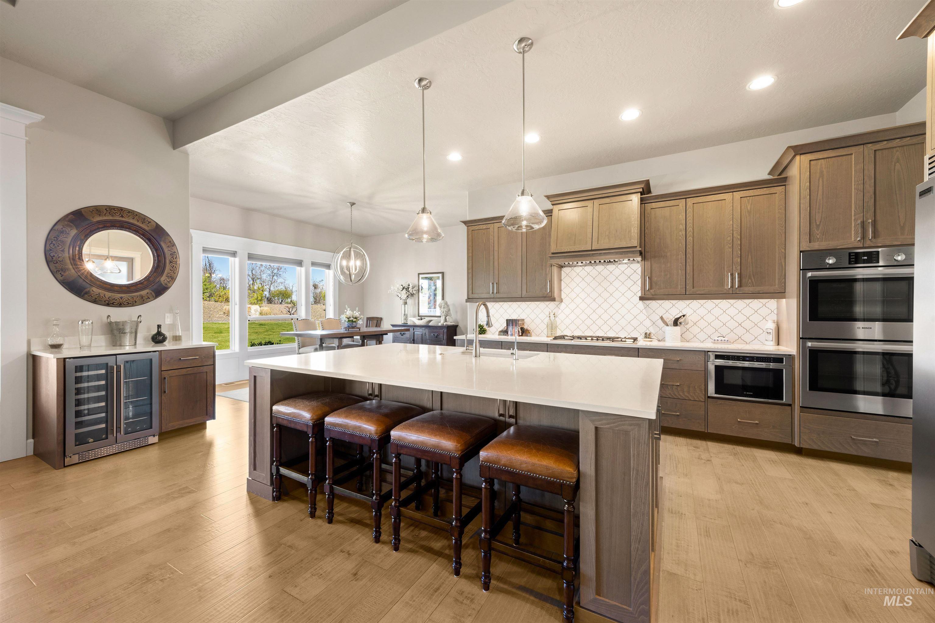 15465 Syrah Court Caldwell, ID 83607 - Photo 14 of 45 Kitchen with beverage cooler, a kitchen bar, decorative backsplash, stainless steel double oven, and hanging light fixtures