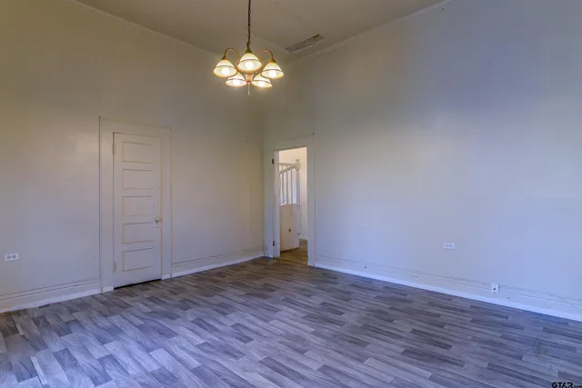 an empty room with wooden floor chandelier and windows