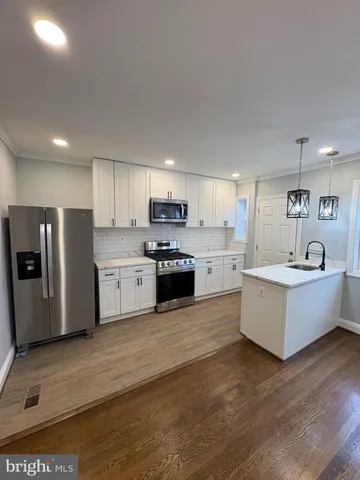 a large kitchen with stainless steel appliances a large counter top a stove a sink dishwasher a refrigerator and white cabinets with wooden floor