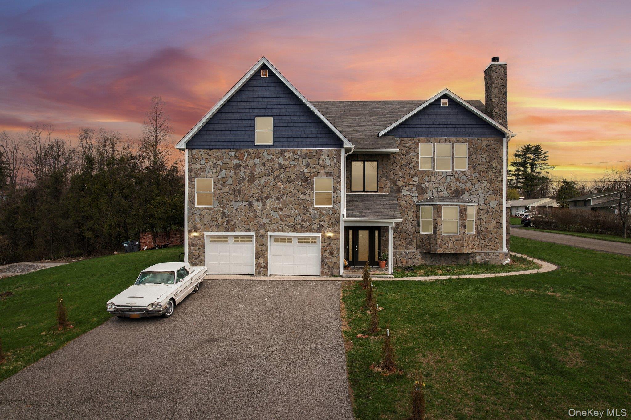 The property features a stone and siding exterior, a prominent stone chimney, a two-car garage, a spacious green lawn.