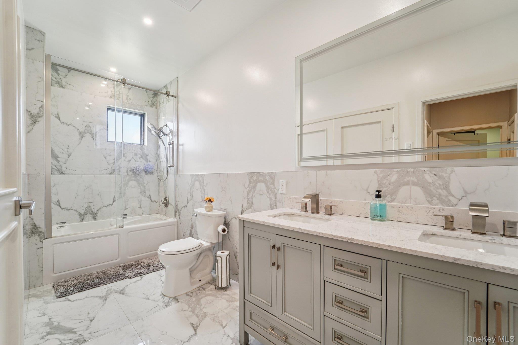 109 Bennett Road Newburgh, NY 12550 - Photo 22 of 41 Bathroom 2: This bathroom features a double vanity with light gray cabinetry and brushed nickel hardware, set against a backdrop of white marble-patterned tile flooring and wall accents. Includes laundry area.