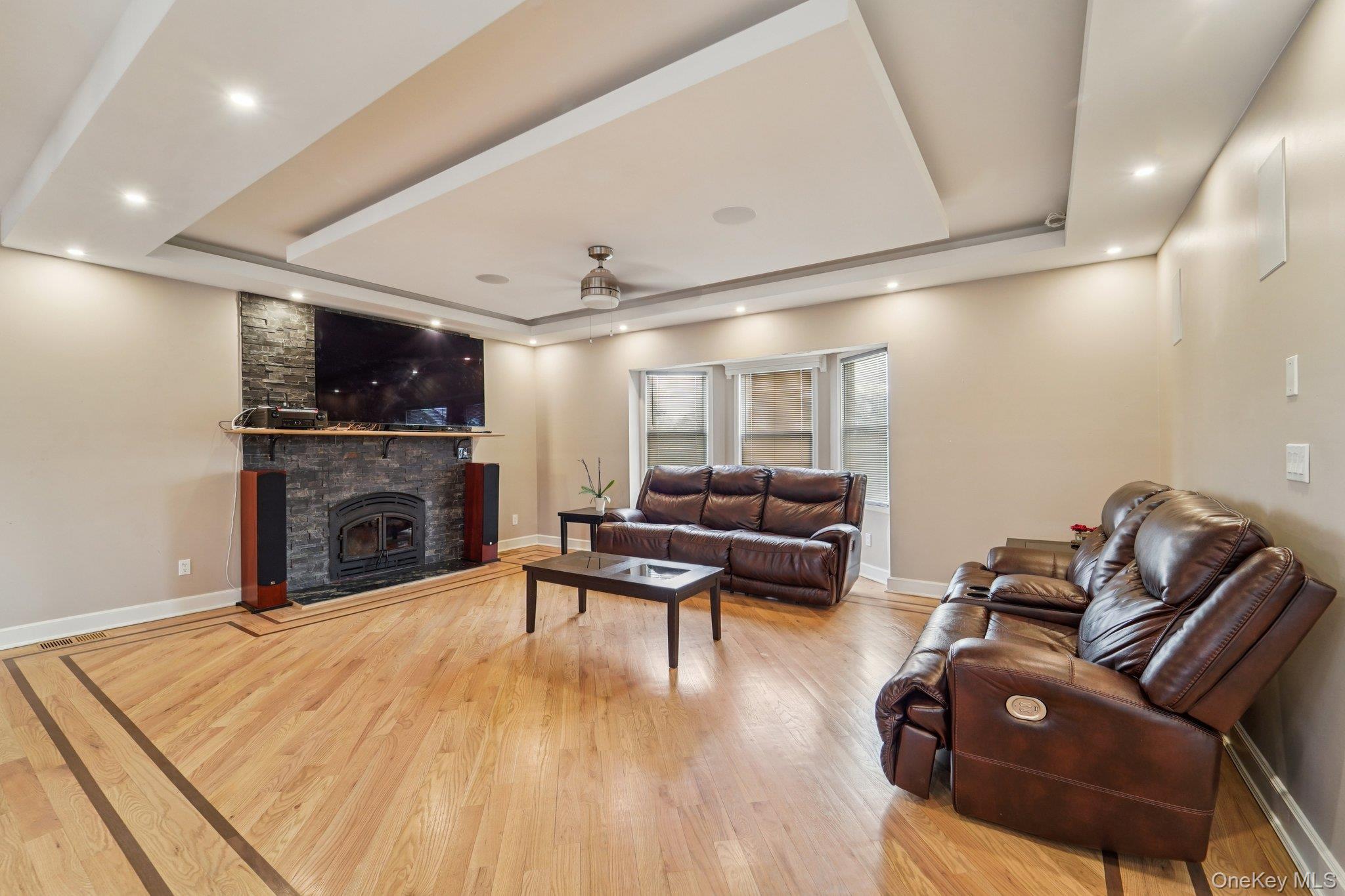 109 Bennett Road Newburgh, NY 12550 - Photo 8 of 41 Living area featuring hardwood flooring with decorative inlay, a stone-clad fireplace, and tray ceilings with recessed lighting.