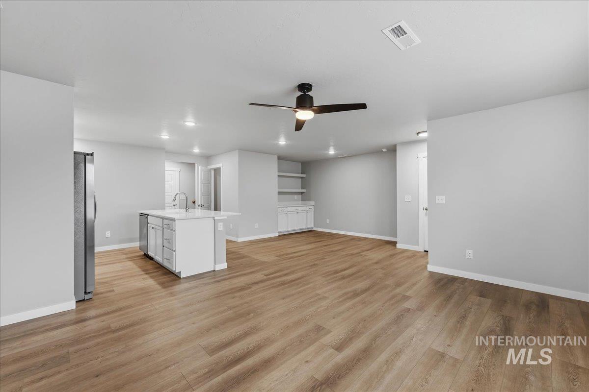 12475 West Victory Road Boise, ID 83709 - Photo 7 of 26 Spacious open-concept area featuring wood-finish flooring, a kitchen island with a sink and white cabinetry, and stainless steel appliances