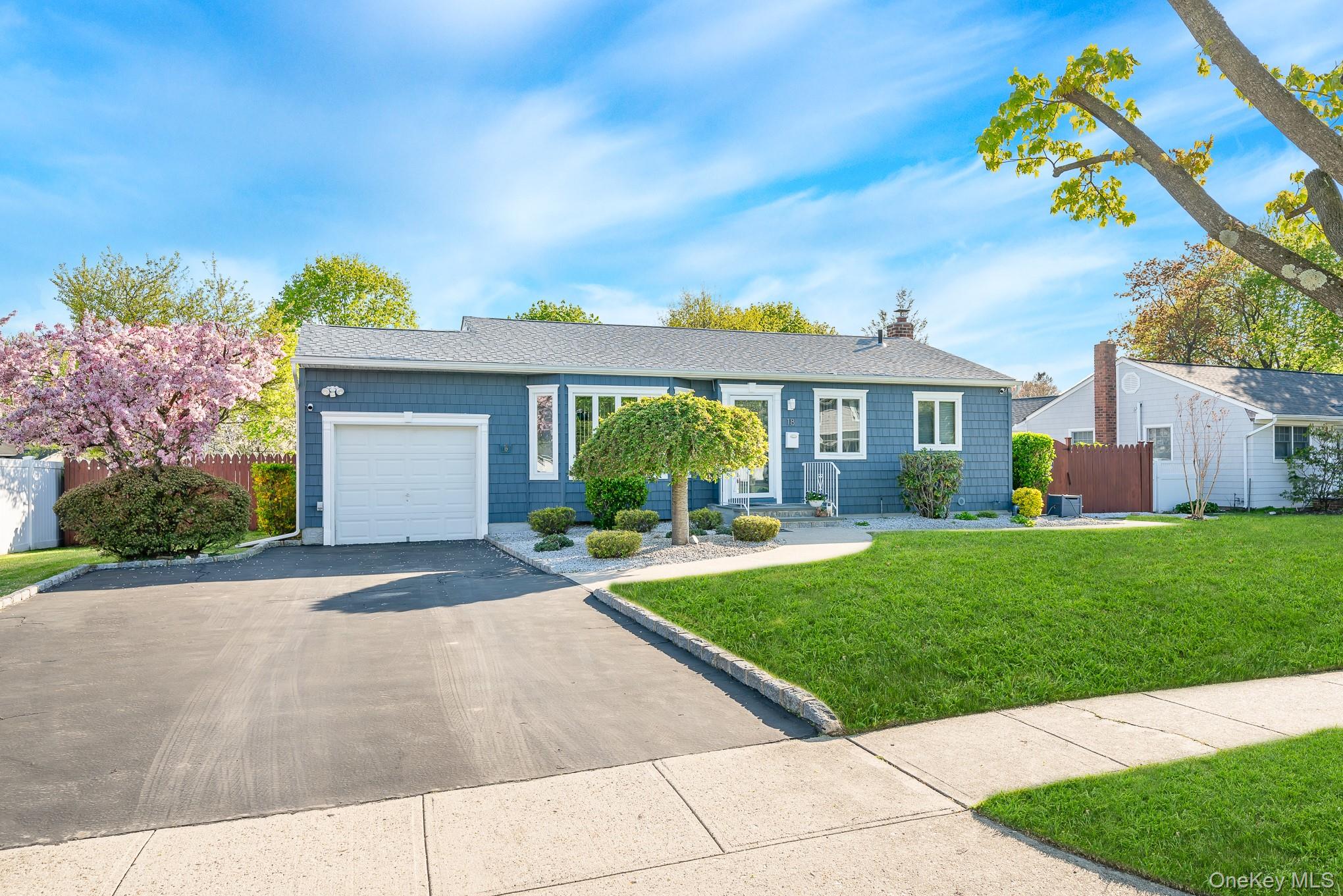 Ranch-style exterior with blue siding, mature trees and a lush green lawn