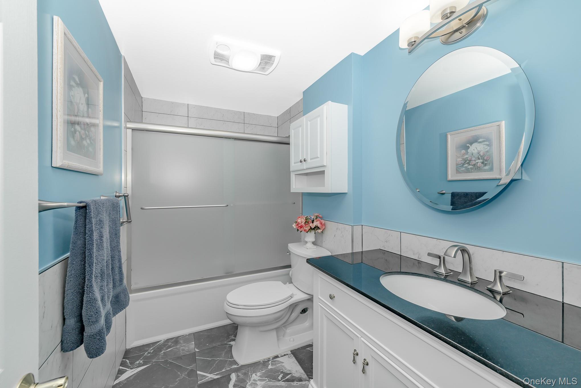 18 Byron Road Commack, NY 11725 - Photo 18 of 32 Bathroom featuring a white vanity with a dark countertop, an oval undermount sink, and a circular wall-mounted mirror