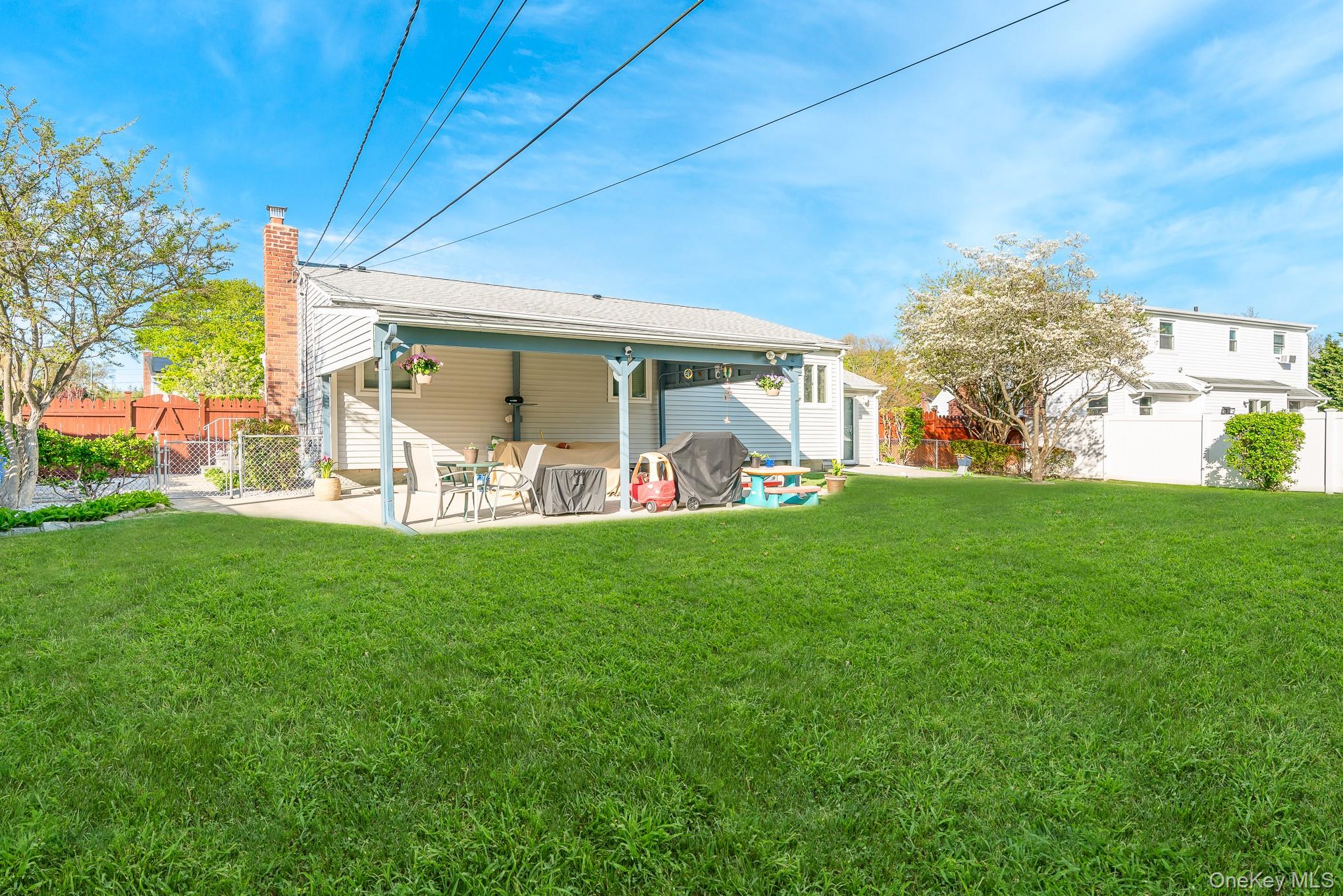 18 Byron Road Commack, NY 11725 - Photo 5 of 32 Expansive lawn with a covered patio featuring light blue columns, a red brick chimney, and privacy fence