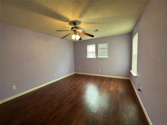 an empty room with wooden floor fan and windows