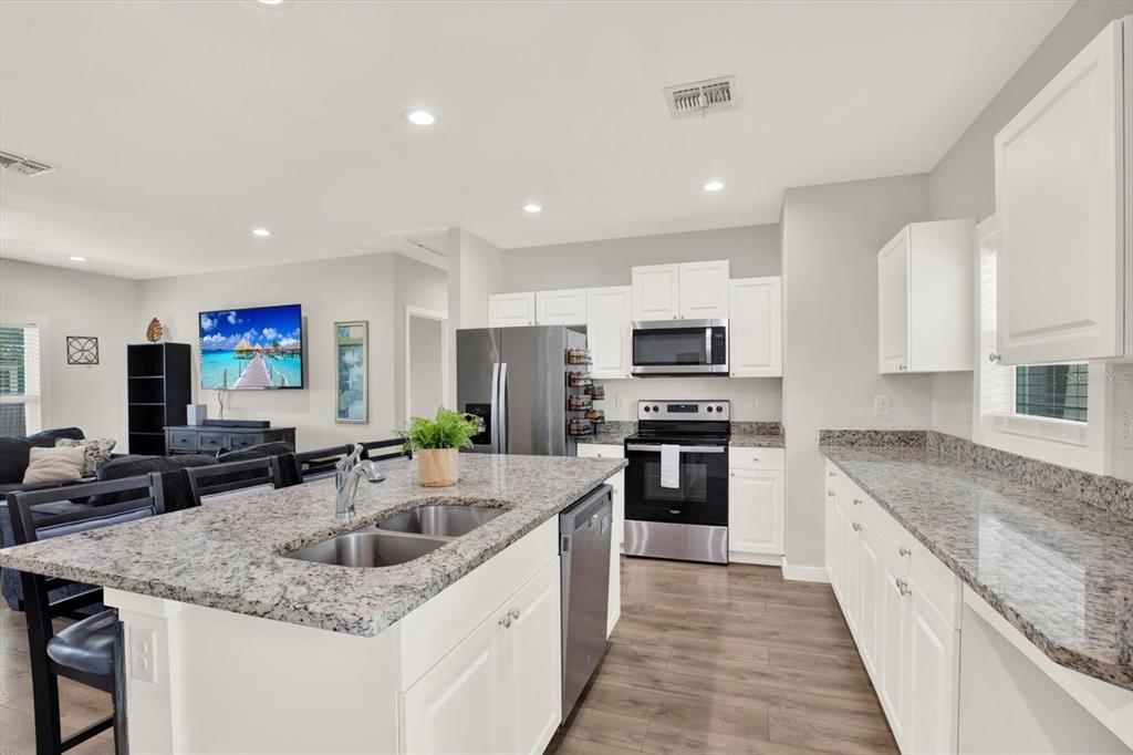 3023 Muir Street Holiday, FL 34691 - Photo 6 of 25 a kitchen with stainless steel appliances granite countertop a sink dishwasher a stove and a refrigerator with wooden floor
