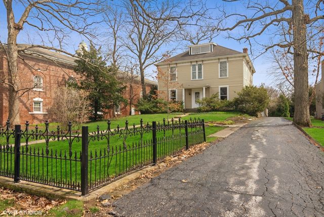 a front view of a house with a yard with plants and large trees