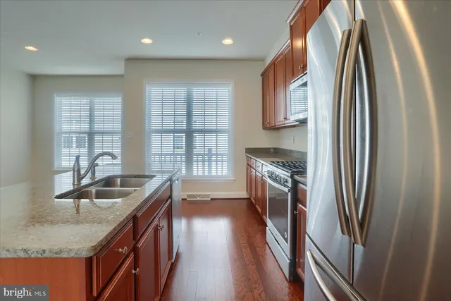 a kitchen with stainless steel appliances granite countertop a refrigerator a sink a stove and a wooden floors