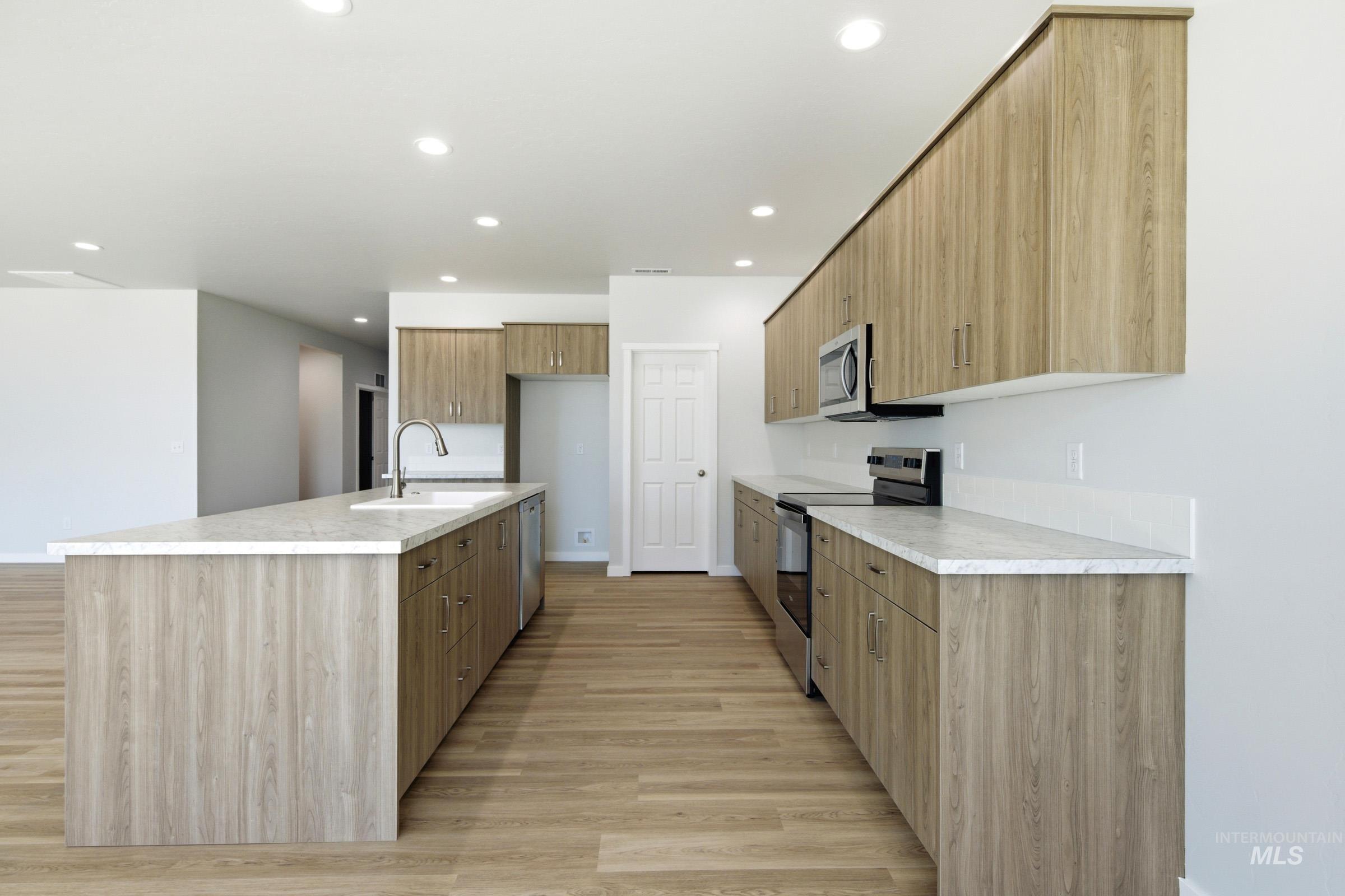 13649 Inman Court Caldwell, ID 83607 - Photo 6 of 22 Modern kitchen featuring light wood-finish cabinetry, stainless steel appliances, a center island with sink, white countertops, and wood-finish flooring