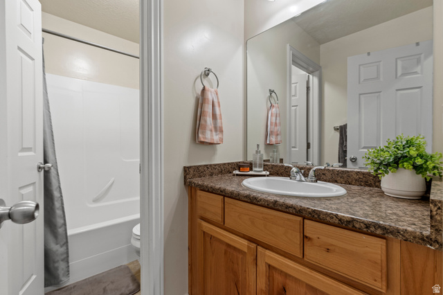 8248 South Resaca Drive, Unit J10 Sandy, UT 84070 - Photo 20 of 40 Bathroom featuring a wood-finish vanity with an integrated sink, a speckled countertop, and a large wall-mounted mirror