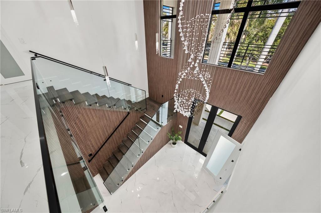 135 7th Street North Naples, FL 34102 - Photo 3 of 50 Every detail has been thoughtfully curated—from oversized tile flooring and soaring ceilings with wood beam and shiplap accents to the modern wood-and-glass floating staircase and grand two-story entry foyer.