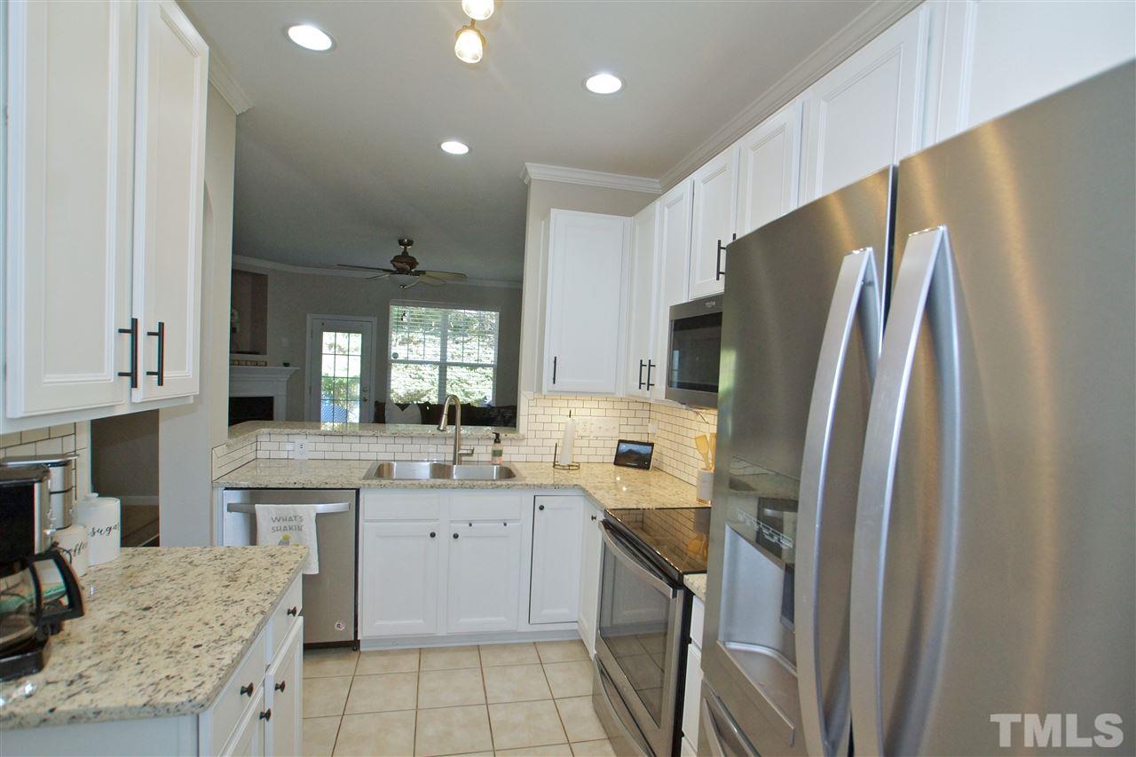 4807 Sir Duncan Way Raleigh, NC 27612 - Photo 14 of 29 a kitchen with stainless steel appliances granite countertop a refrigerator a sink a stove and white cabinets with wooden floor