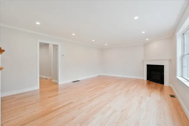 a view of an empty room with wooden floor and a fireplace