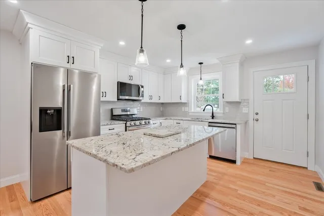 a kitchen with stainless steel appliances granite countertop a refrigerator a sink a stove and a wooden floor