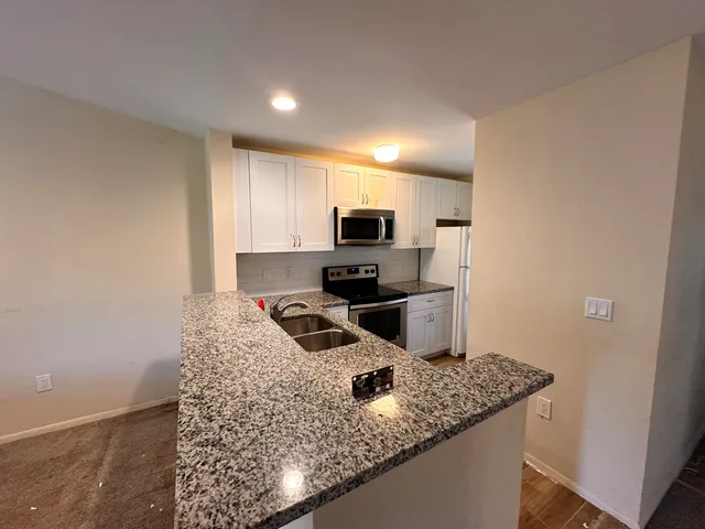 a kitchen with granite countertop a sink a stove top oven a counter space and cabinets