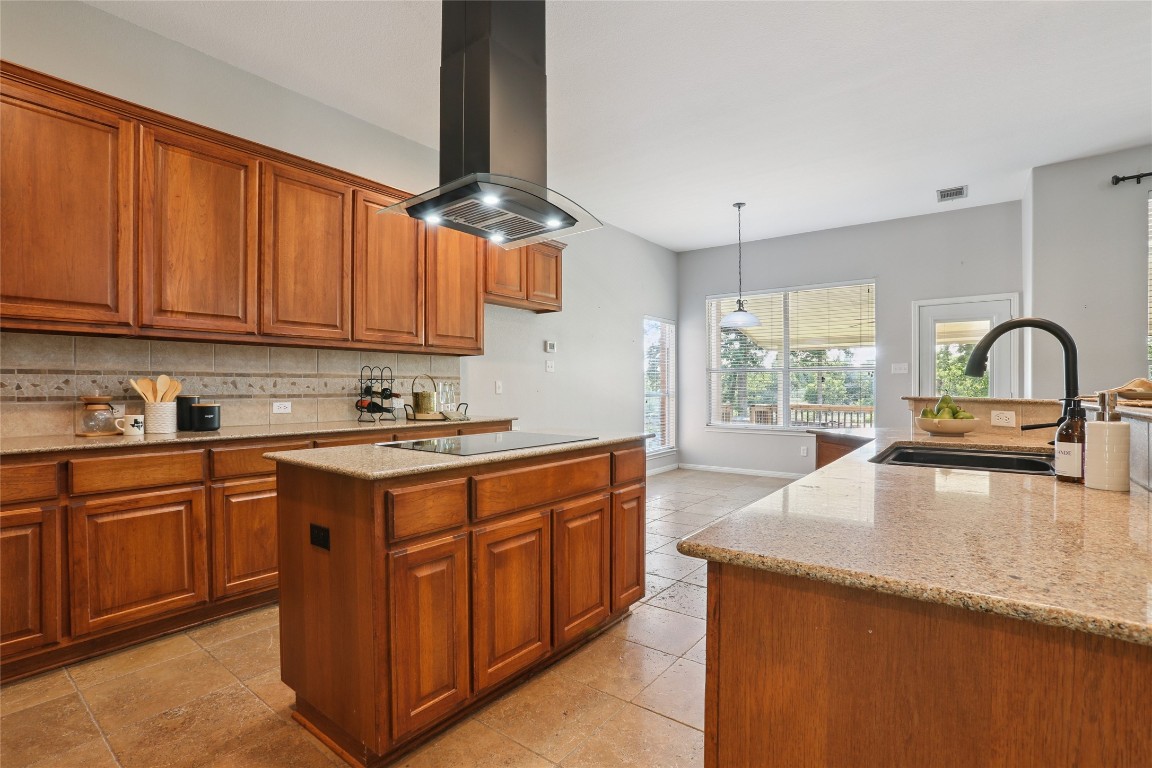 120 Juniper Trail Elgin, TX 78621 - Photo 5 of 32 Kitchen with light stone countertops, brown cabinets, tasteful backsplash, a center island, and island range hood