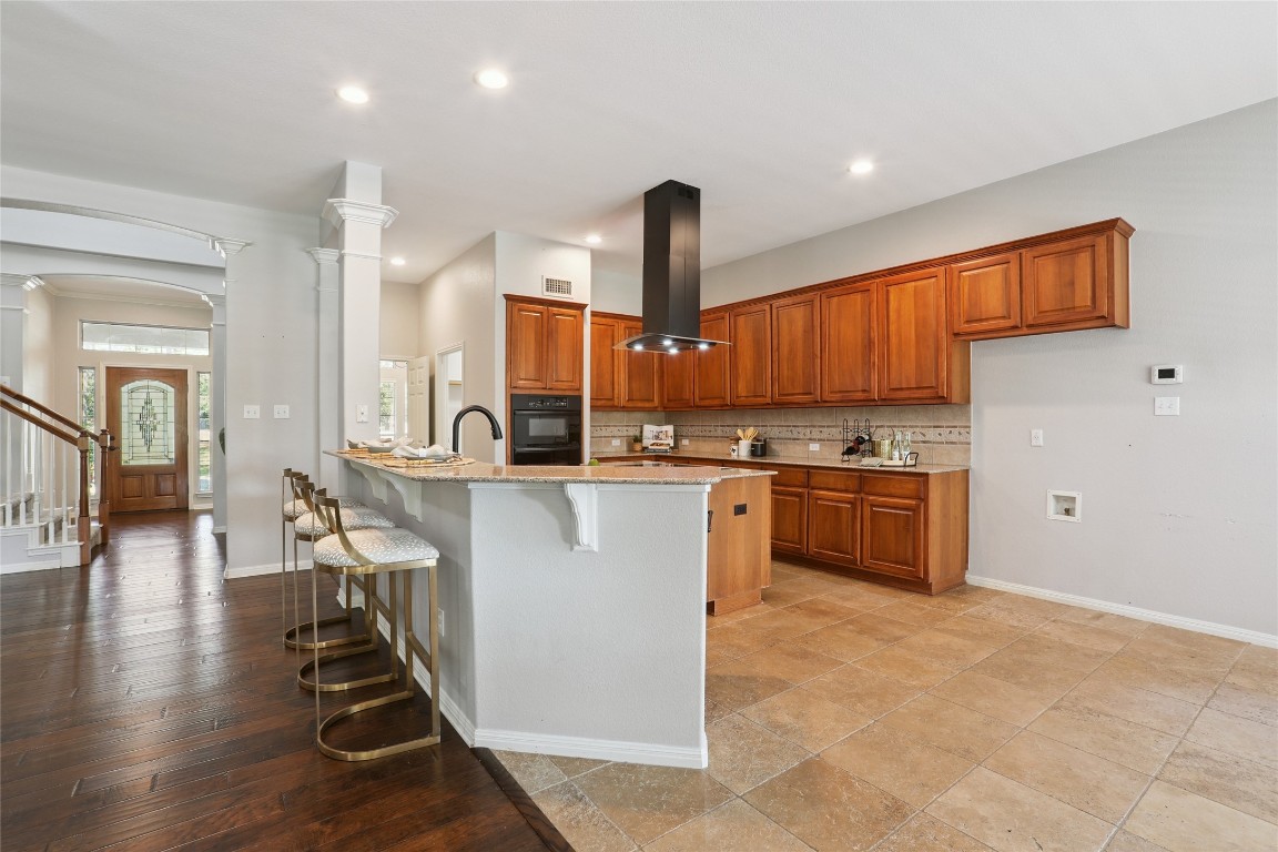 120 Juniper Trail Elgin, TX 78621 - Photo 6 of 32 Kitchen featuring a breakfast bar area, brown cabinets, decorative backsplash, light stone countertops, and island exhaust hood