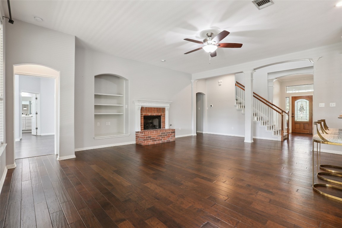 120 Juniper Trail Elgin, TX 78621 - Photo 9 of 32 Unfurnished living room featuring arched walkways, built in shelves, decorative columns, and dark wood-style flooring