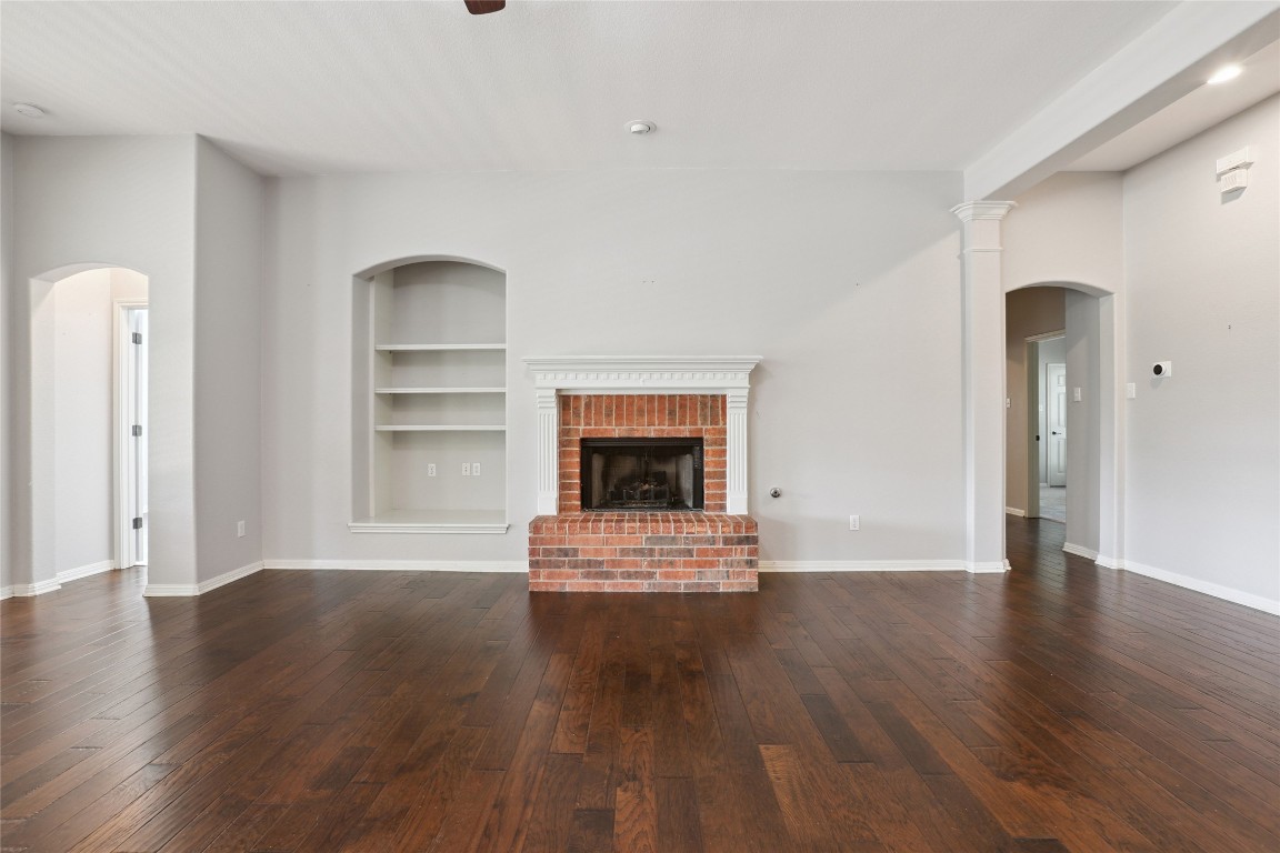 120 Juniper Trail Elgin, TX 78621 - Photo 10 of 32 Unfurnished living room featuring arched walkways, dark wood finished floors, a brick fireplace, built in features, and recessed lighting