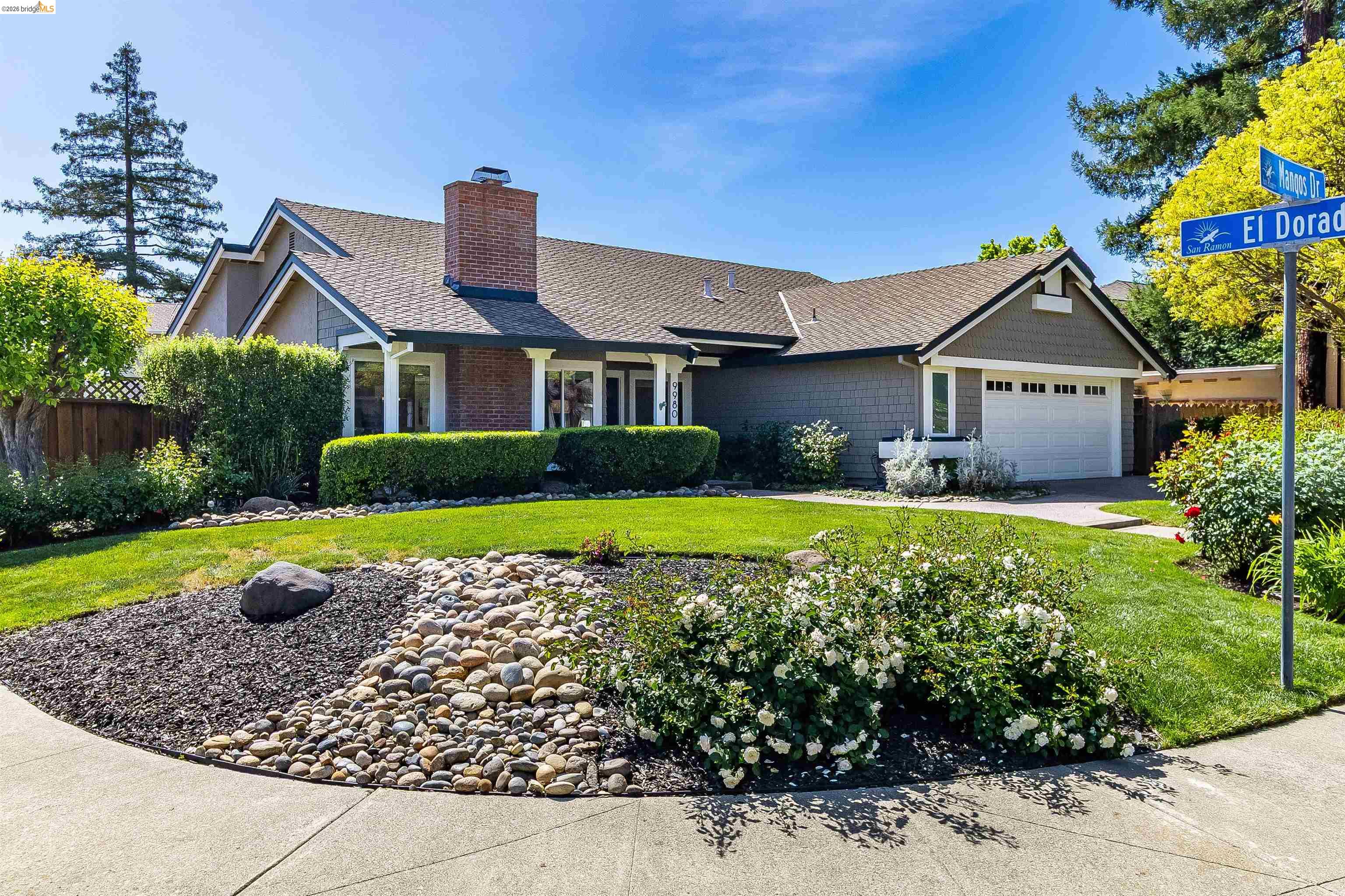 View of front facade featuring a chimney, an attached garage, driveway, and roof with shingles