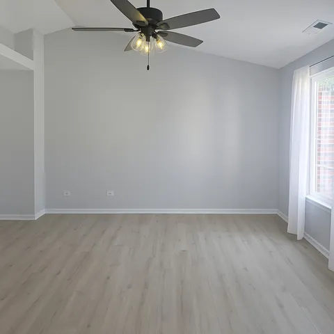 an empty room with wooden floor fan and windows
