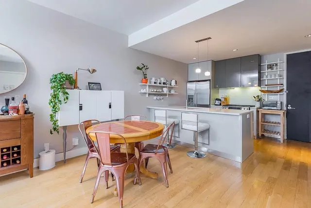 a kitchen with stainless steel appliances kitchen island granite countertop a dining table chairs and a refrigerator