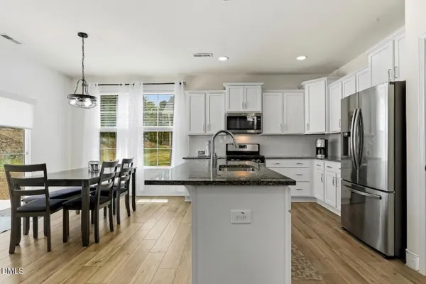 a kitchen with stainless steel appliances granite countertop a refrigerator a stove top oven a sink dishwasher a dining table and chairs with wooden floor