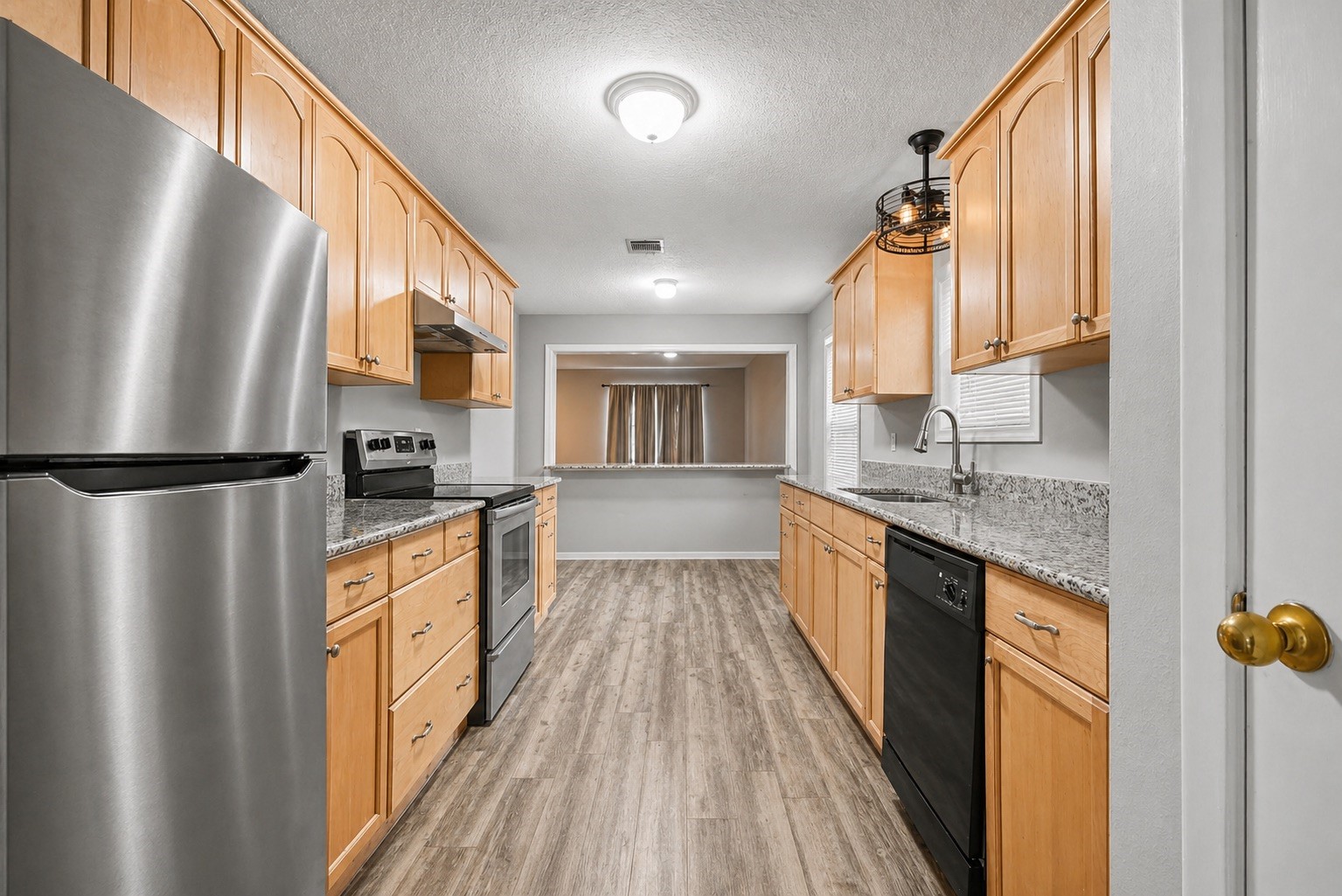 a kitchen with stainless steel appliances granite countertop a refrigerator a sink dishwasher a stove and a dining table with wooden floor