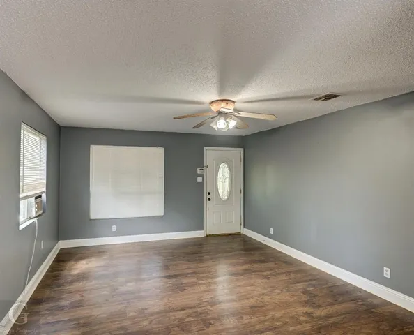 an empty room with wooden floor chandelier and windows