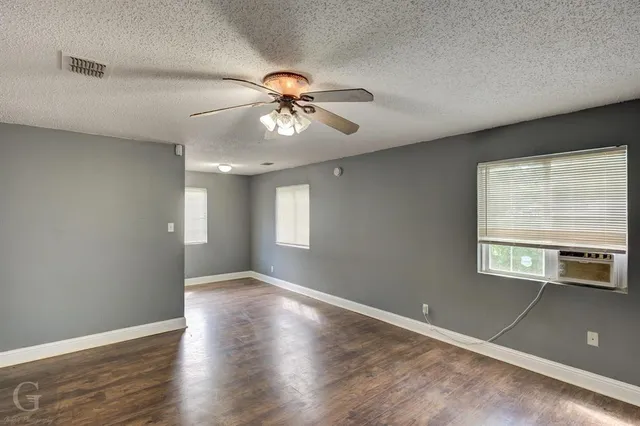 an empty room with wooden floor chandelier fan and windows