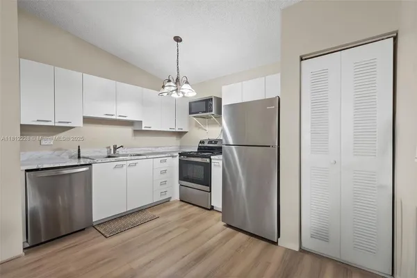 a kitchen with stainless steel appliances granite countertop a refrigerator a sink dishwasher a stove and white cabinets with wooden floor