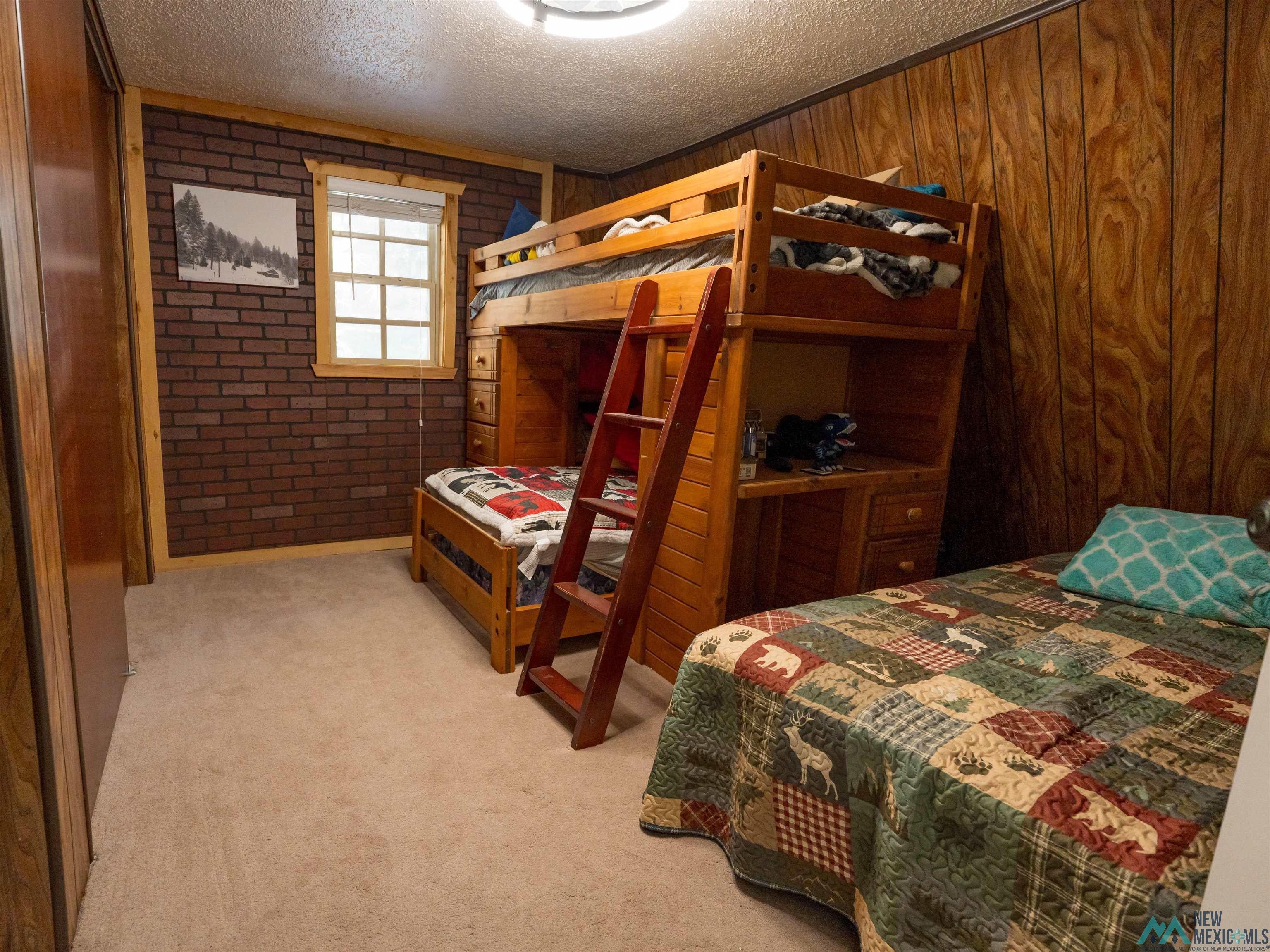 3 Wimsatt Road Cloudcroft, NM 88317 - Photo 28 of 41 Bedroom featuring brick wall, light colored carpet, and a textured ceiling