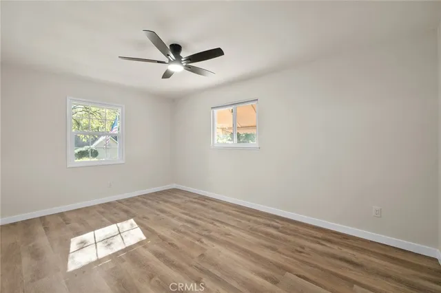 an empty room with wooden floor ceiling fan and windows