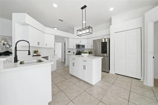 a kitchen with stainless steel appliances a sink a stove a refrigerator cabinets a dining table and chairs