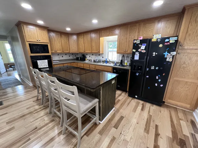 a kitchen with stainless steel appliances kitchen island granite countertop a refrigerator a stove a sink and a dining table with wooden floor