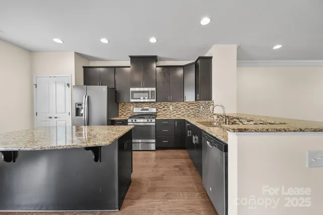 a large kitchen with stainless steel appliances kitchen island granite countertop a refrigerator and a sink