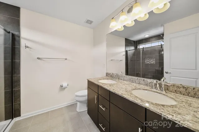 a bathroom with a granite countertop double vanity sink mirror and toilet