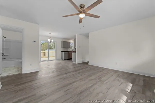 an empty room with wooden floor chandelier fan and windows