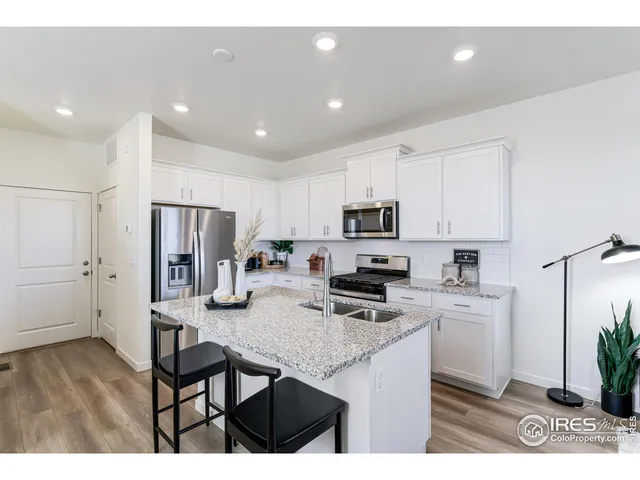 a kitchen with stainless steel appliances kitchen island granite countertop a refrigerator a stove a sink dishwasher and white cabinets with wooden floor