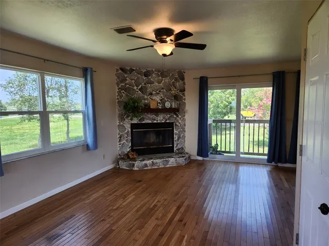 a view of an empty room with wooden floor fireplace and a window