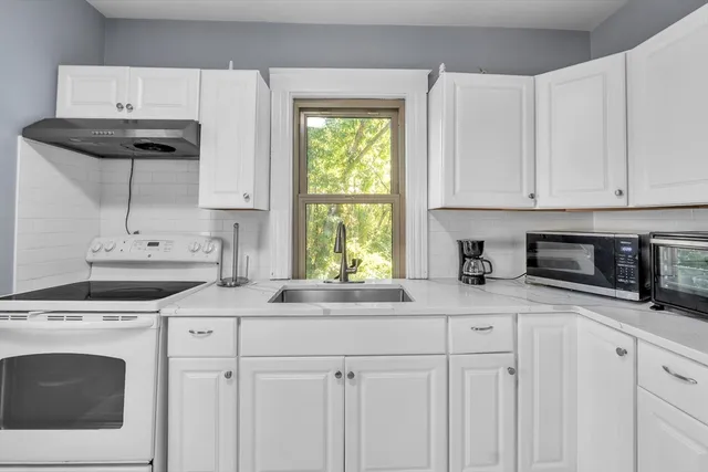 a kitchen with granite countertop white cabinets white appliances and a sink