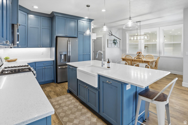 1009 High Creek Road Cove, UT 84320 - Photo 19 of 79 Kitchen featuring blue cabinets, a breakfast bar area, light stone countertops, a center island with sink, and pendant lighting