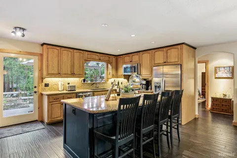 a kitchen with stainless steel appliances granite countertop a stove top oven a sink dishwasher a dining table and chairs with wooden floor