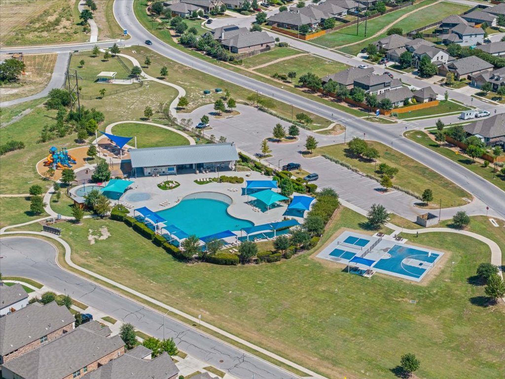 277 Spinnaker Loop Kyle, TX 78640 - Photo 36 of 38 An aerial perspective reveals a vibrant community hub with a sparkling pool, recreation center, and playful basketball court.