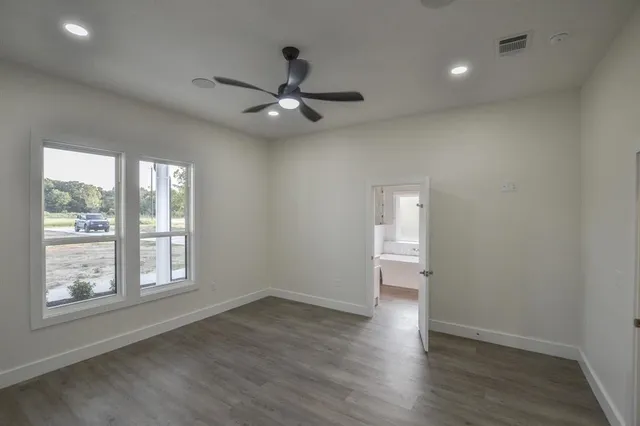 an empty room with wooden floor fan and windows