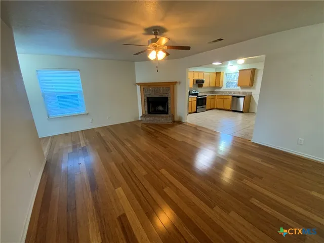 a view of an empty room with wooden floor fireplace and a window
