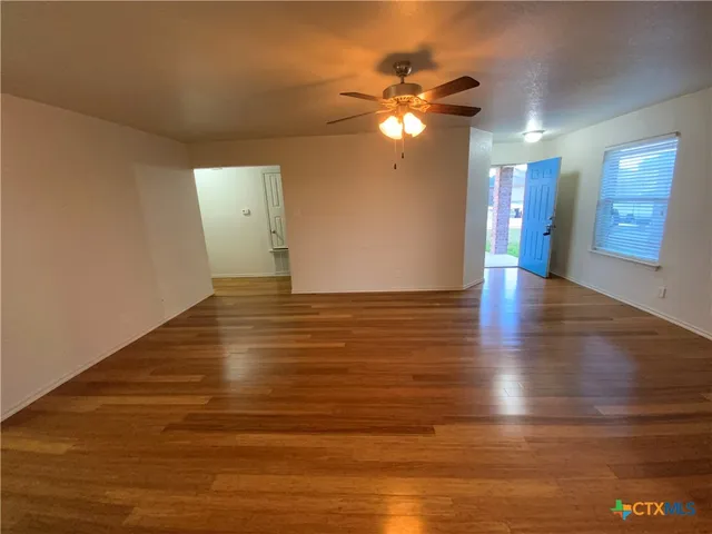 a view of an empty room with wooden floor and a fan