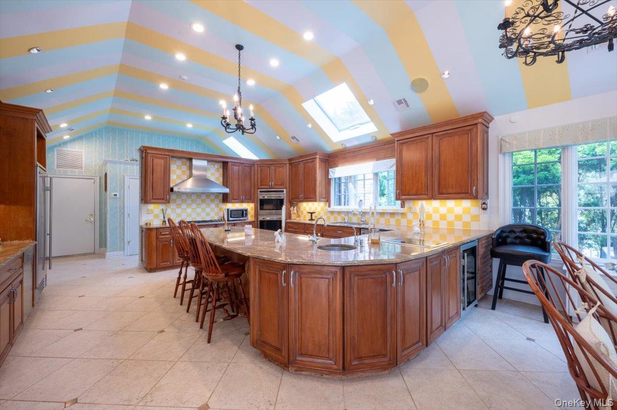 1331 Harbor Road Hewlett, NY 11557 - Photo 14 of 50 Kitchen featuring backsplash, a chandelier, brown cabinetry, light stone counters, and vaulted ceiling